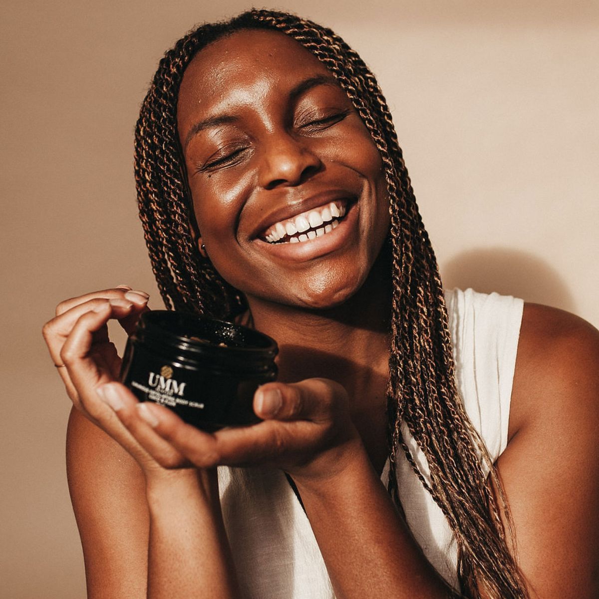 Black woman smiling holding UMM Skincare's body scrub to gently exfoliate her skin.