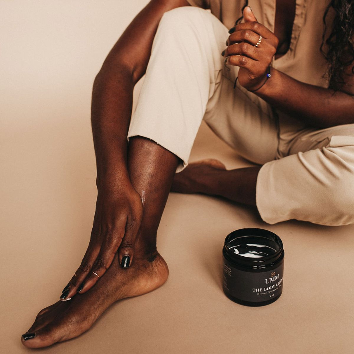 Woman with dark skin applying UMM Skincare Body Cream to her legs and feet.