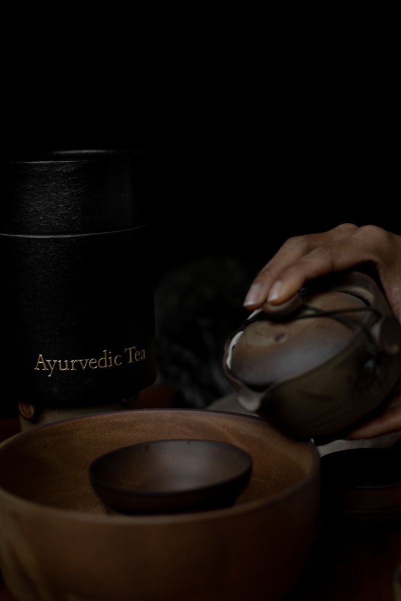 Brewing tea with a traditional bronze Ayurvedic teapot and cup.