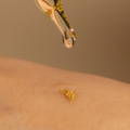Body oil dropper with gold flaked oil on woman's skin. 