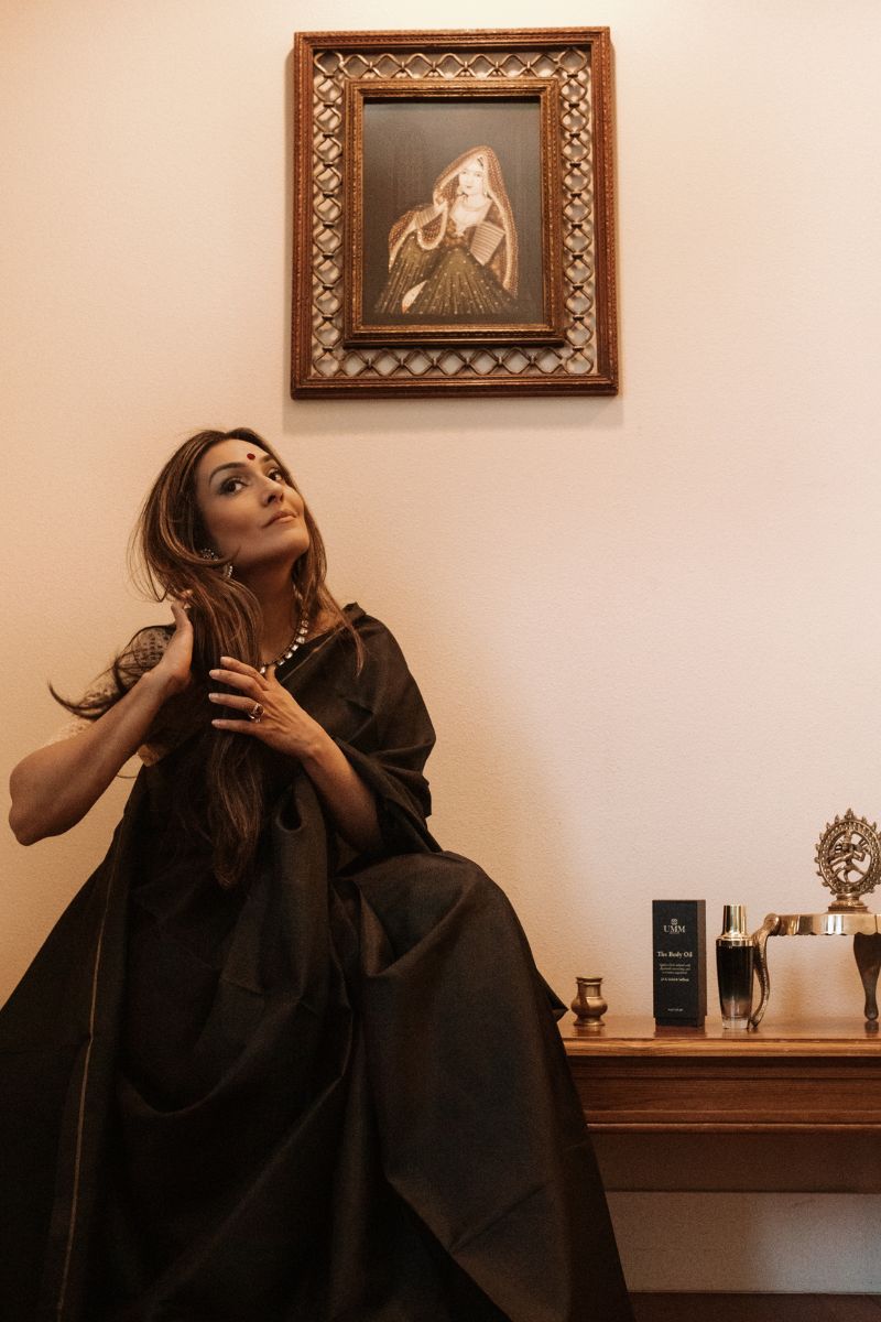 UMM Skincare founder Anisha Vinjamuri, seated next to UMM Skincare products and traditional Indian art work.
