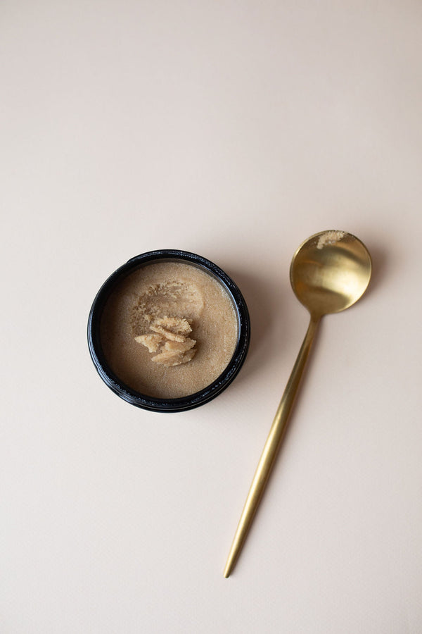 Gold spoon with UMM Skincare Body Scrub next to it with an earthy color and corse texture. 