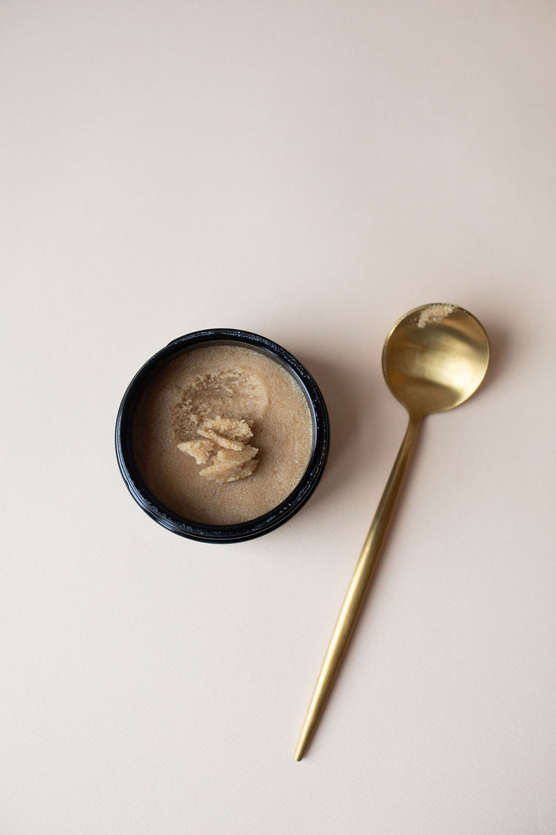 Gold spoon with UMM Skincare Body Scrub next to it with an earthy color and corse texture. 